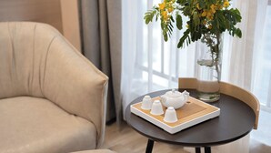 En moderne stue med en beige sofa, et lille rundt bord med en bakke hvide tepotter og en vase med gule blomster.
