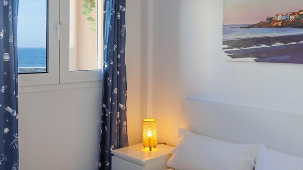 Un dormitorio con cama, una mesita de noche con lámpara, una ventana con cortinas y un cuadro en la pared.