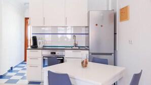 Cocina compacta con armarios blancos, refrigerador de acero inoxidable y comedor con dos sillas y una mesa.
