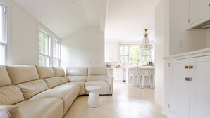 A spacious living room with a beige sectional sofa, a small white table, and a kitchen area with white cabinets and bar stools. - Spacious 5-bedroom house with pool and two office rooms in charming Montclair (Montclair)