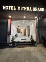 The entrance of Hotel Mithra Grand with a reception desk, seating area, and potted plants.