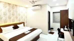 A hotel room with a bed, a desk, a chair, a ceiling fan, an air conditioning unit, and a window. - HOTEL MITHRA GRAND (Hyderabad)