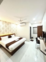 A hotel room with a bed, a desk, a chair, a ceiling fan, an air conditioning unit, and a window.