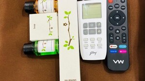 A remote control, a bottle of green liquid, and two boxes on a brown fabric surface. - HOTEL MITHRA GRAND (Hyderabad)