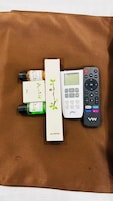 Un control remoto, una botella con líquido verde y dos cajas sobre una superficie de tela marrón.