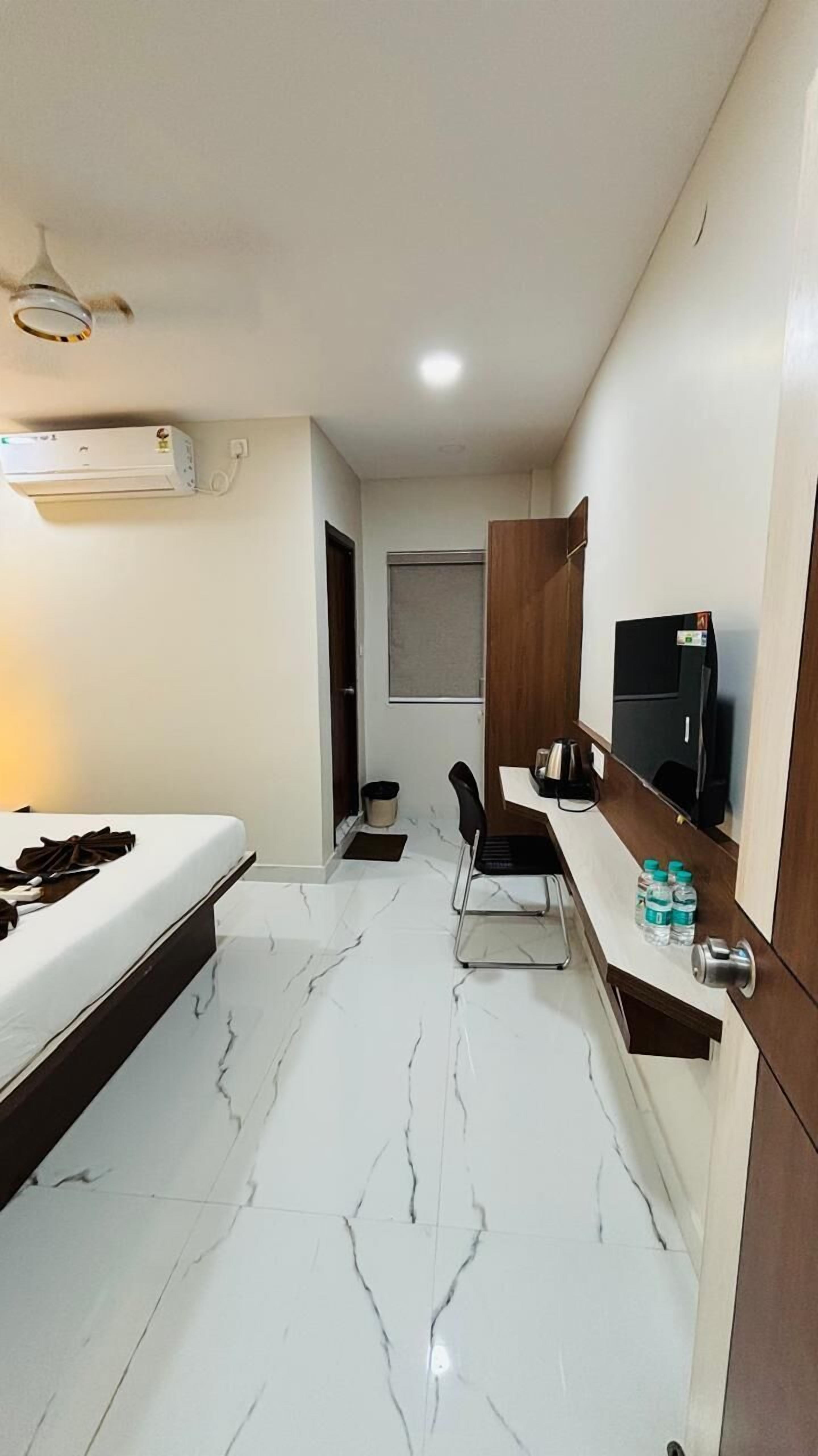 A hotel room with a bed, a desk with a chair, a television, and an air conditioning unit.