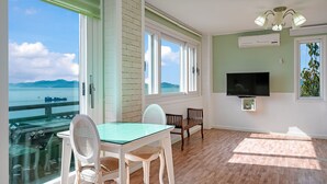 Une pièce dotée d’une grande fenêtre donnant sur un plan d’eau, d’un téléviseur fixé au mur et d’une table à manger avec des chaises.