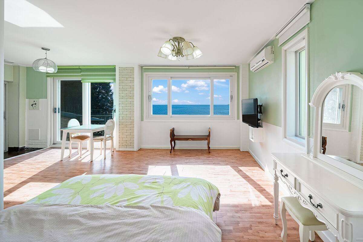 Ein Schlafzimmer mit Bett, Sitzbank, Fernseher und großem Fenster mit Meerblick.