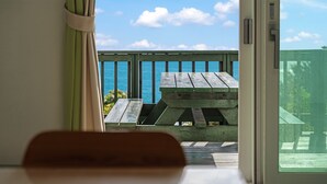 Vue depuis l’intérieur d’une pièce sur une terrasse extérieure avec une table en bois et une balustrade donnant sur la mer.