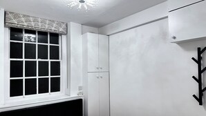 Une chambre à coucher avec un lit, une fenêtre ornée d’un rideau à motifs, une armoire et un porte-manteau fixé au mur.