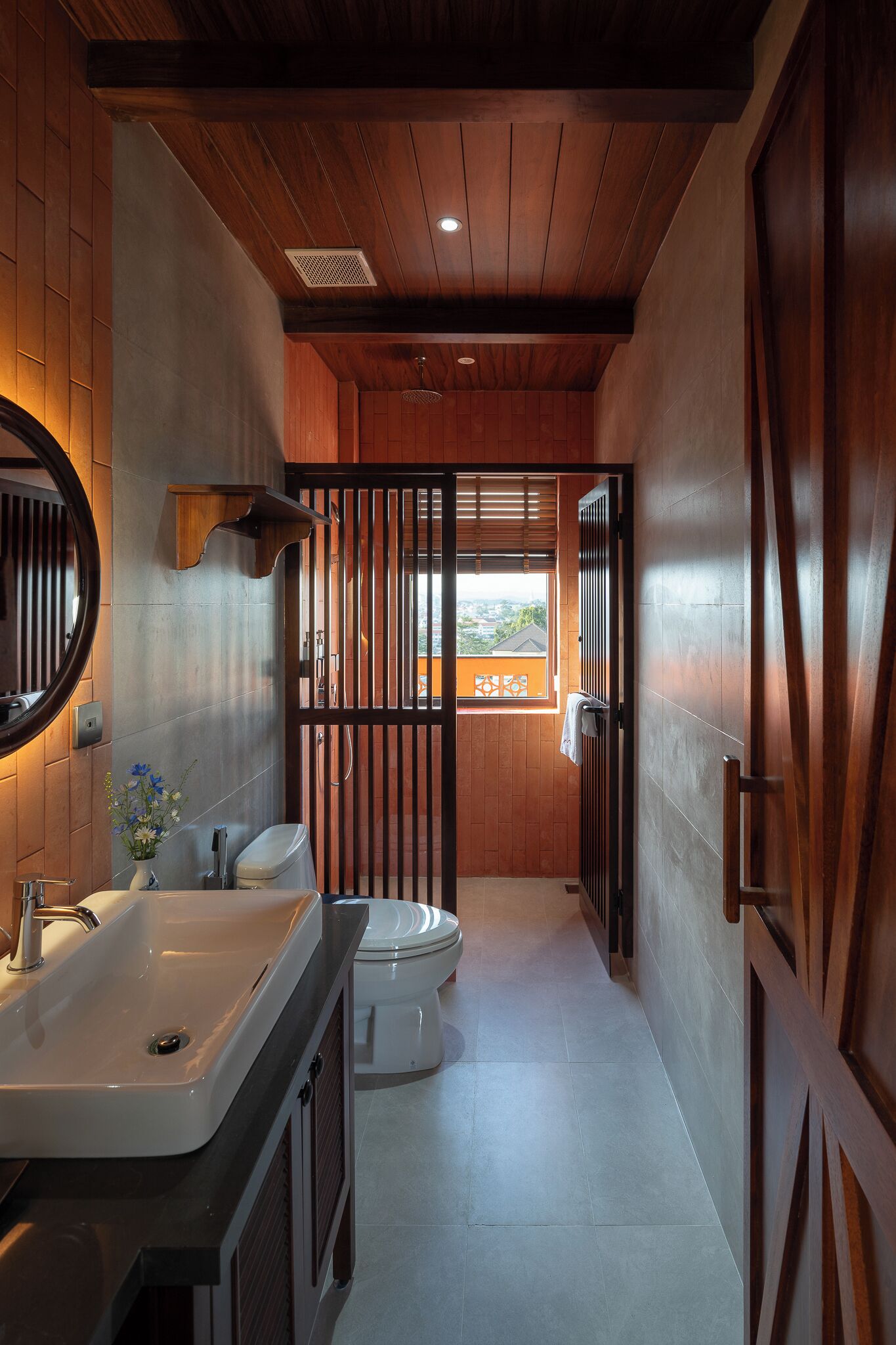 A bathroom with a wooden ceiling, a sink, a toilet, and a window with a view.