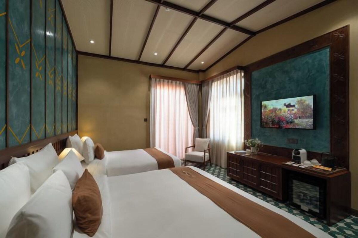 Une chambre d’hôtel avec deux lits, un téléviseur fixé au mur, un bureau avec une chaise et une fenêtre avec des rideaux.