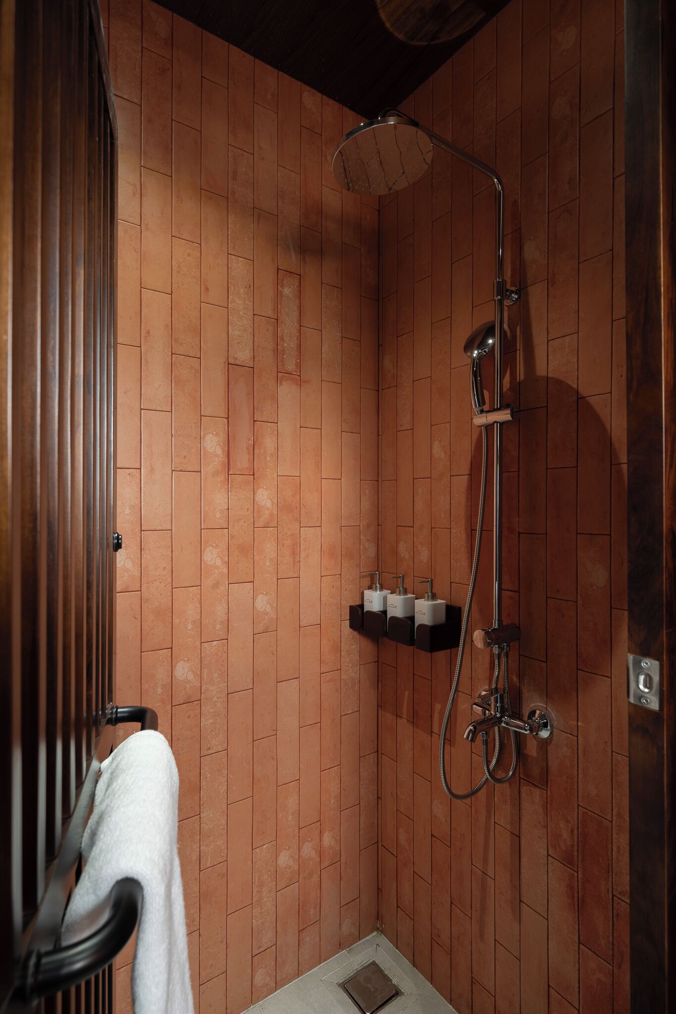 A shower with a handheld showerhead and a wall-mounted faucet. There is a towel rack with a towel hanging on it.
