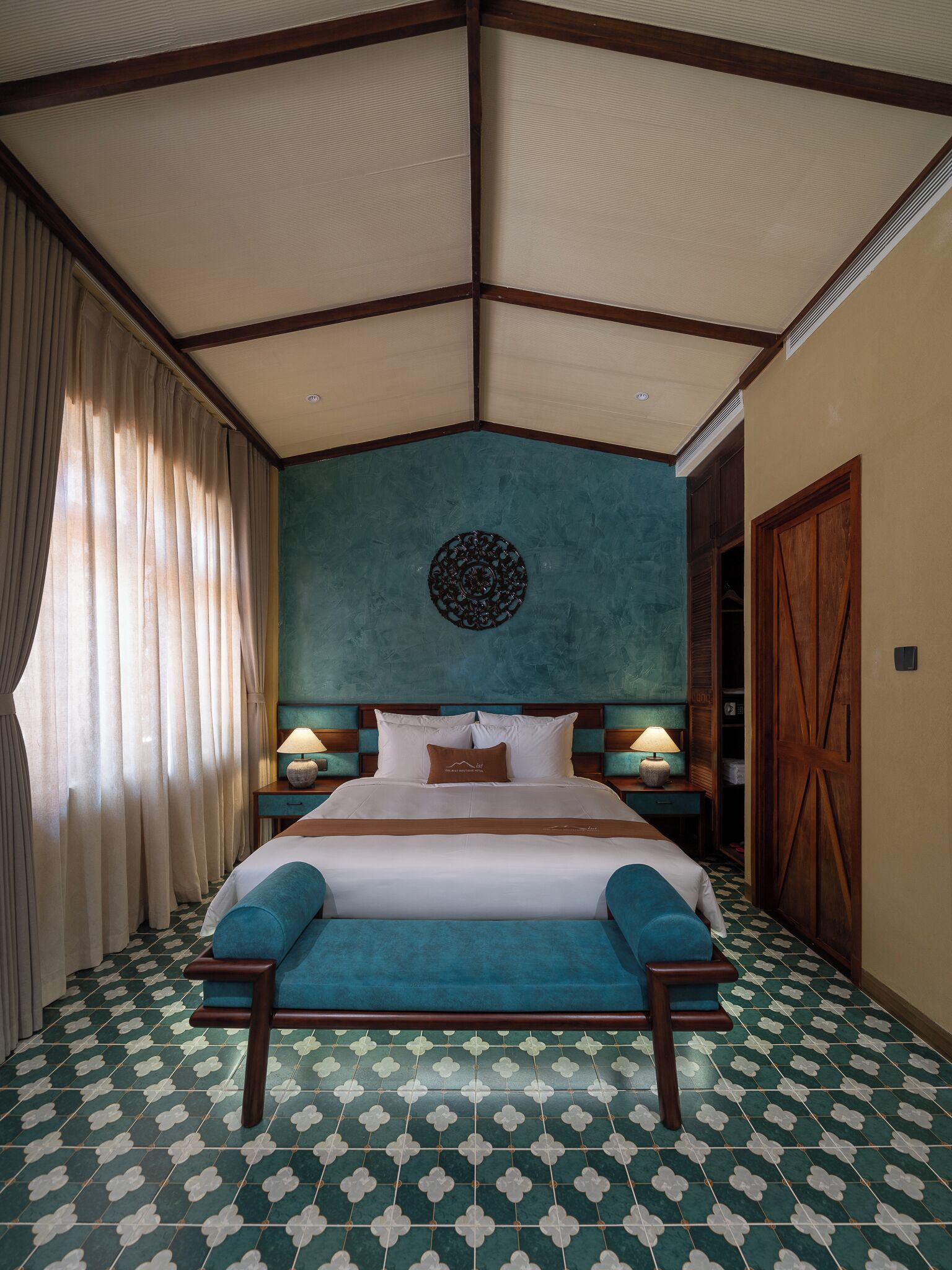 Habitación de hotel con una cama grande, dos mesitas de noche con lámparas, un armario de madera y un suelo estampado.
