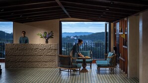 A reception area with a stone counter, two wooden chairs, a table, and a balcony with a view of the mountains.