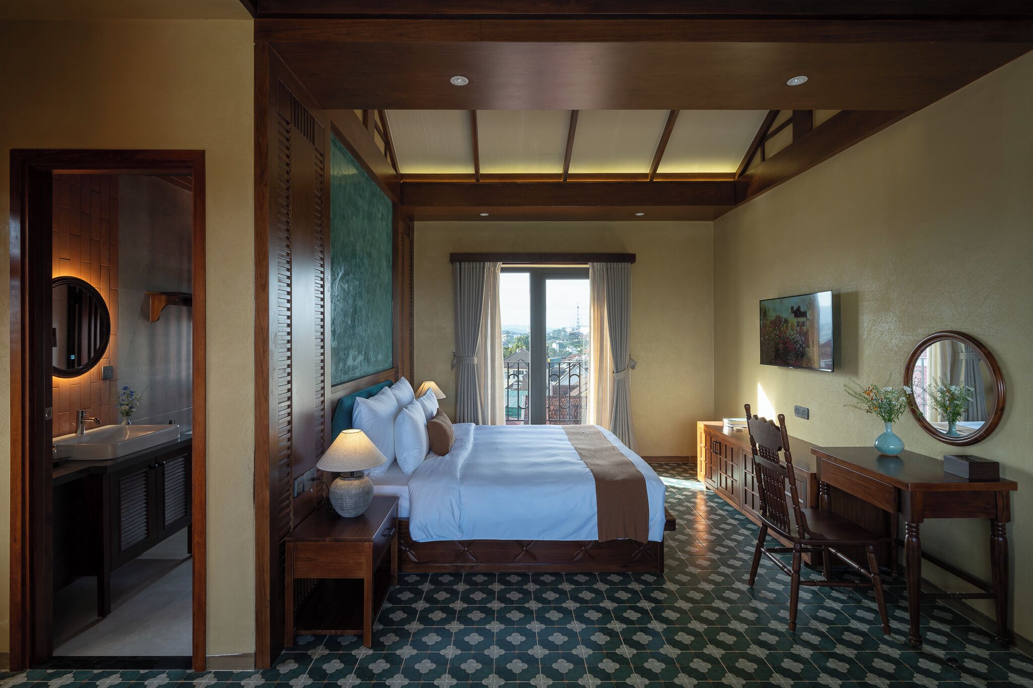 A hotel room with a large bed, a desk, a chair, a vanity with a mirror, and a view of the outdoors through a window.