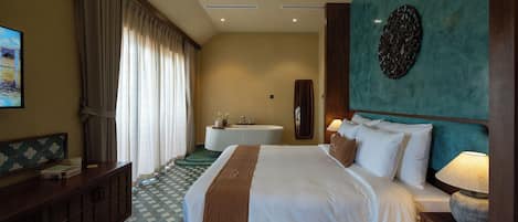 Habitación de hotel con una cama grande, una mesita de noche con lámpara, un tocador con espejo y una ventana con cortinas.