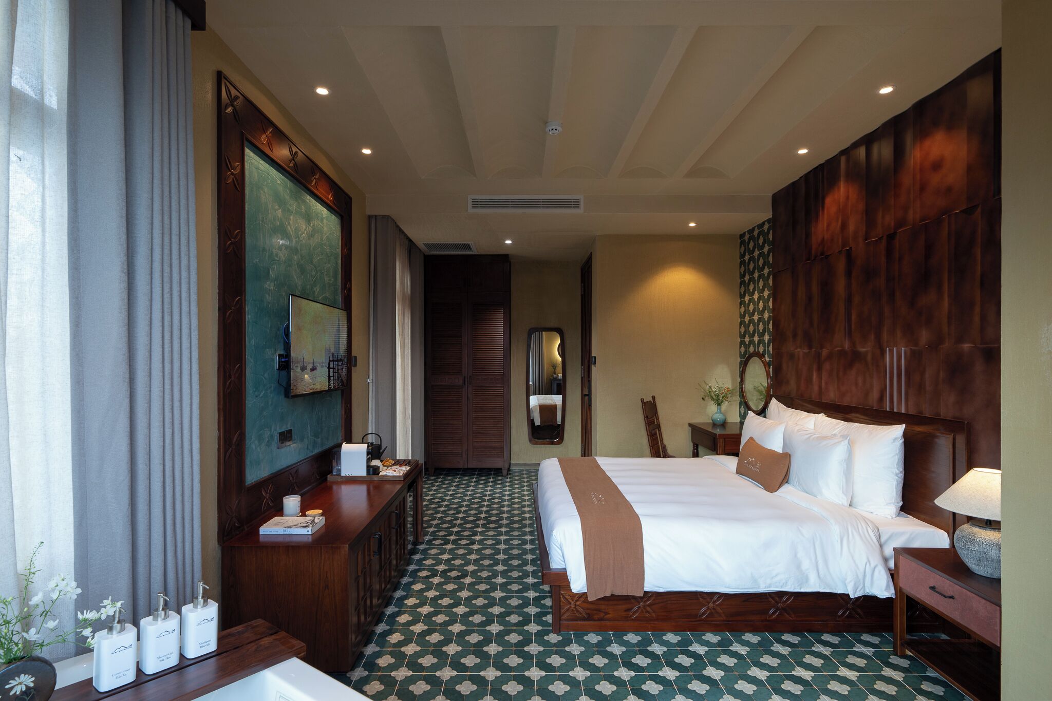 A hotel room with a large bed, a desk with a computer, a TV, and a bathroom with a sink and toiletries.