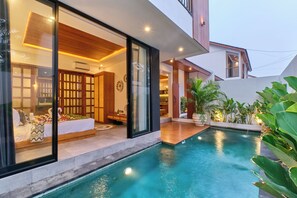A modern house with a swimming pool, a well-lit interior, and a view of the surrounding greenery. - Villa Dharman A1 (Ubud)