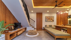 Un salon moderne doté d’un escalier en bois, d’un téléviseur à écran plat, d’un canapé, d’un coin repas et d’un ventilateur de plafond.