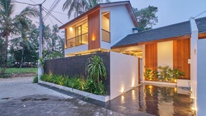 Une maison moderne à deux étages, dotée d’un balcon, d’une allée carrossable et entourée de verdure.