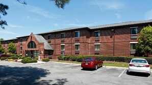 A multi-story brick building with a parking lot and two cars parked in front.