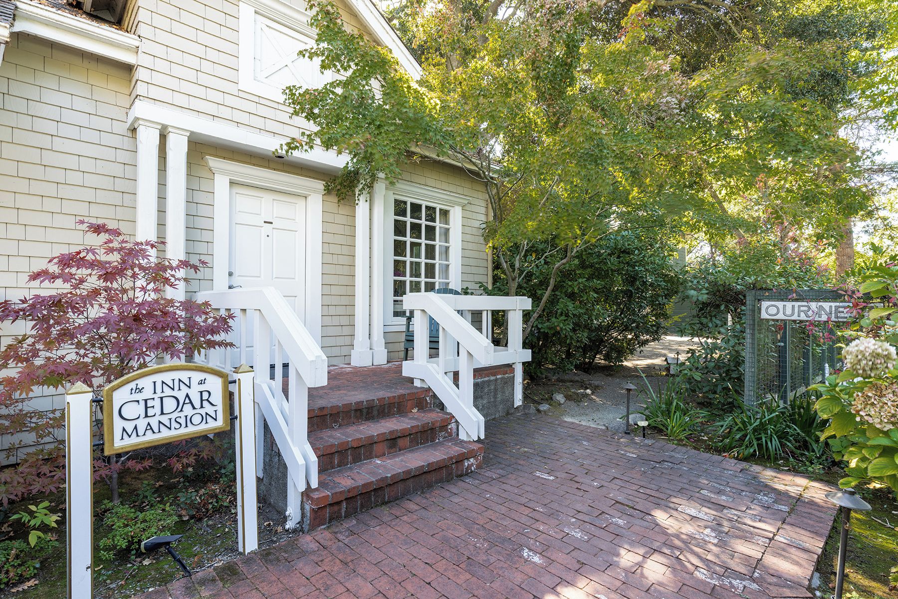 A brick pathway leading to a white building with a porch and a sign for 'The Inn at Cedar Mansion'.