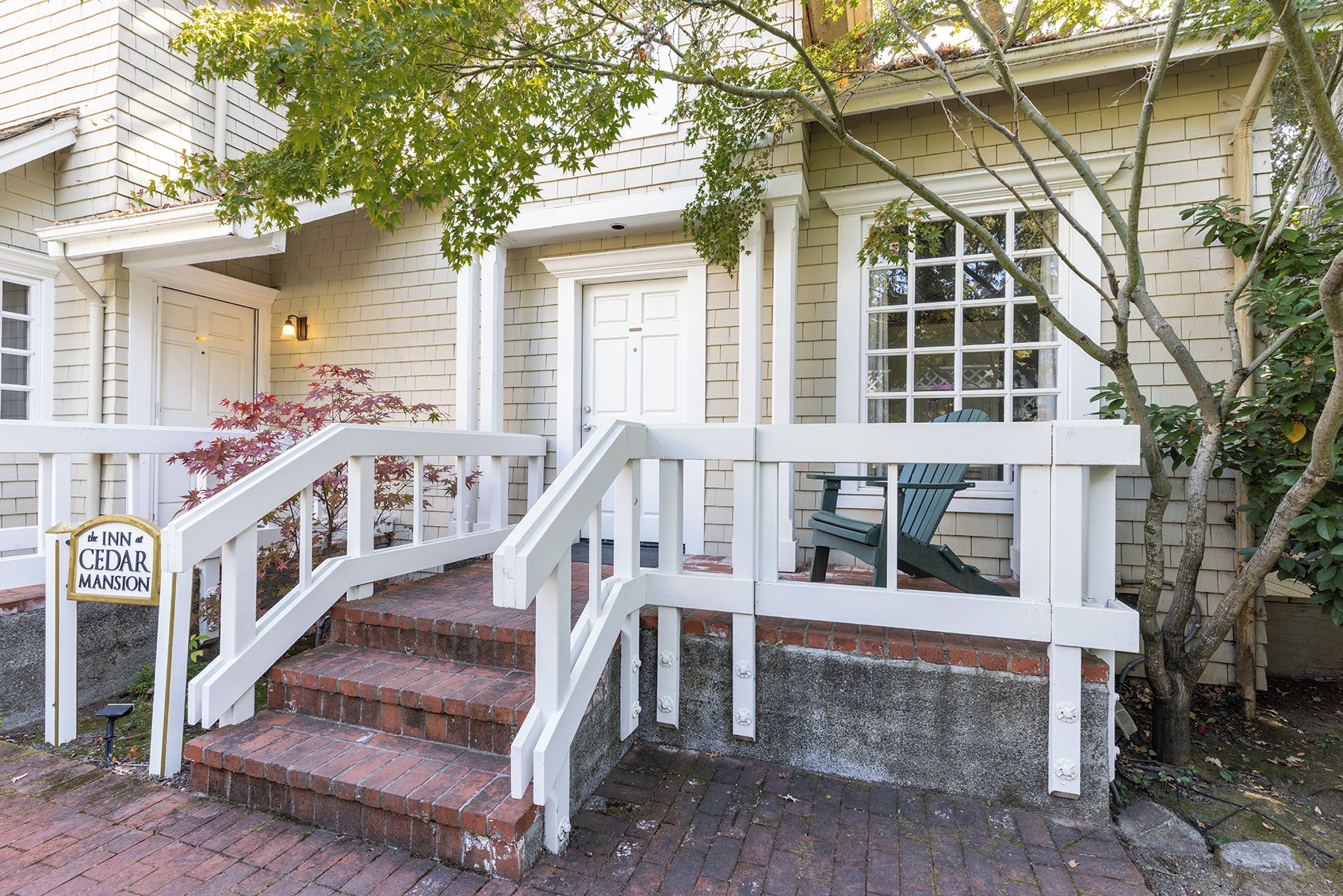 A building with a white exterior, a brick staircase, and a sign indicating 'The Inn at Cedar Mansion.'