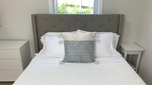 A neatly made bed with a quilted white mattress, a grey upholstered headboard, and two bedside tables with white drawers. - Exclusive Escape- 1 mile to metro w/ FULL kitchen! (McLean)