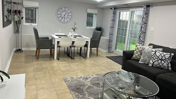 A modern living room with a dining area, featuring a glass coffee table, a black sofa with patterned cushions, and a dining table with four chairs. - Exclusive Escape- 1 mile to metro w/ FULL kitchen! (McLean)