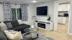 A modern living room with a sofa, coffee table, and TV. There is a kitchen area with cabinets and appliances visible through an open doorway. - Exclusive Escape- 1 mile to metro w/ FULL kitchen! (McLean)