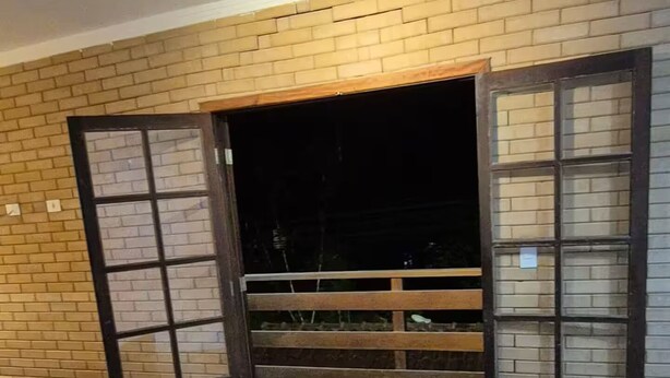 Une pièce avec un plancher en bois, un lit, un mur en briques et une fenêtre avec un cadre en bois.