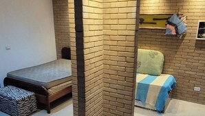 Une chambre moderne avec un mur d’accent en briques, un lit recouvert d’une couverture bleue et blanche, et un banc en bois.