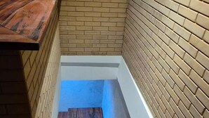 Un escalier étroit avec des marches en bois et des murs en briques, menant à un palier.