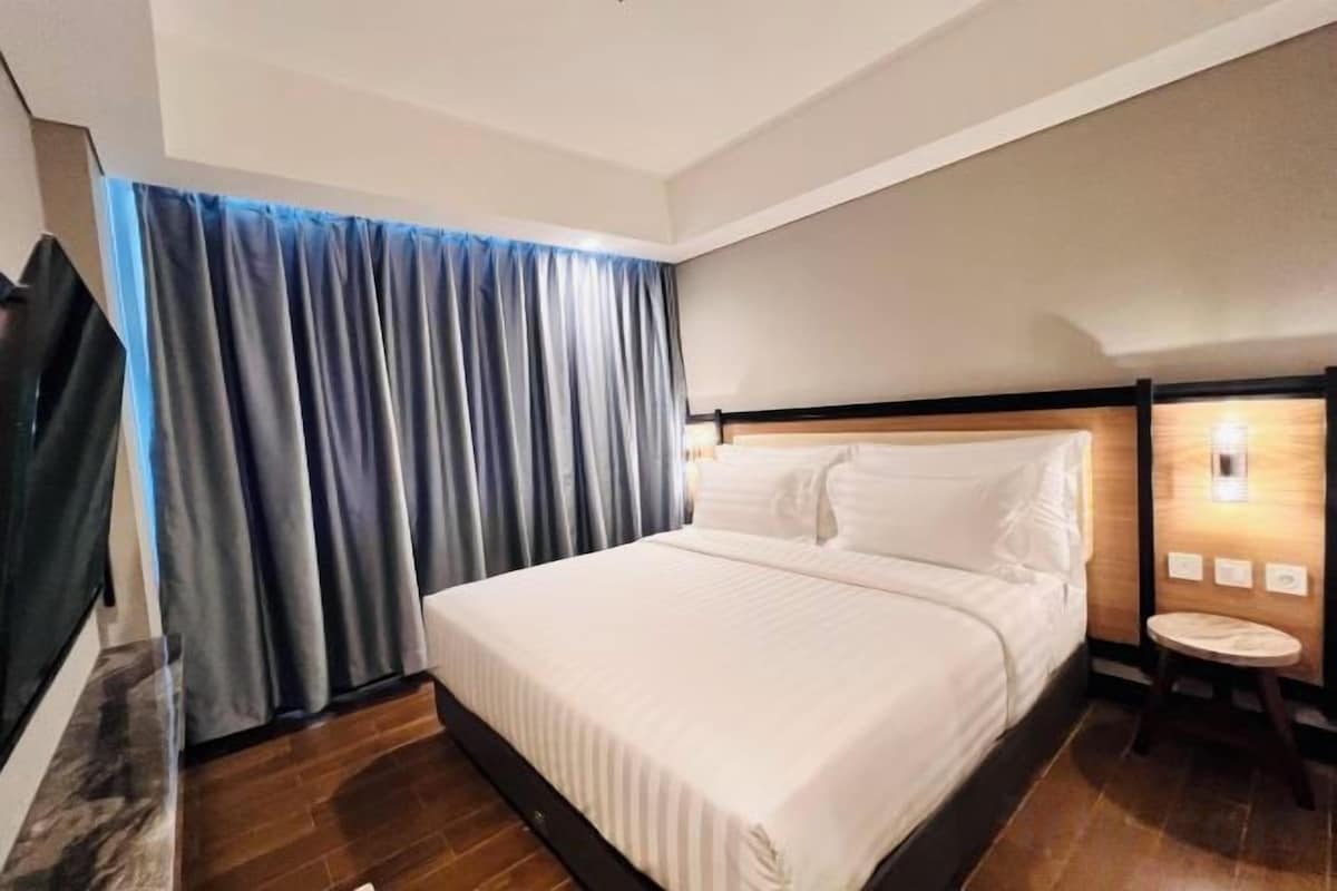 Una habitación de hotel con una cama, cortinas, una mesita de noche y una lámpara de pared.