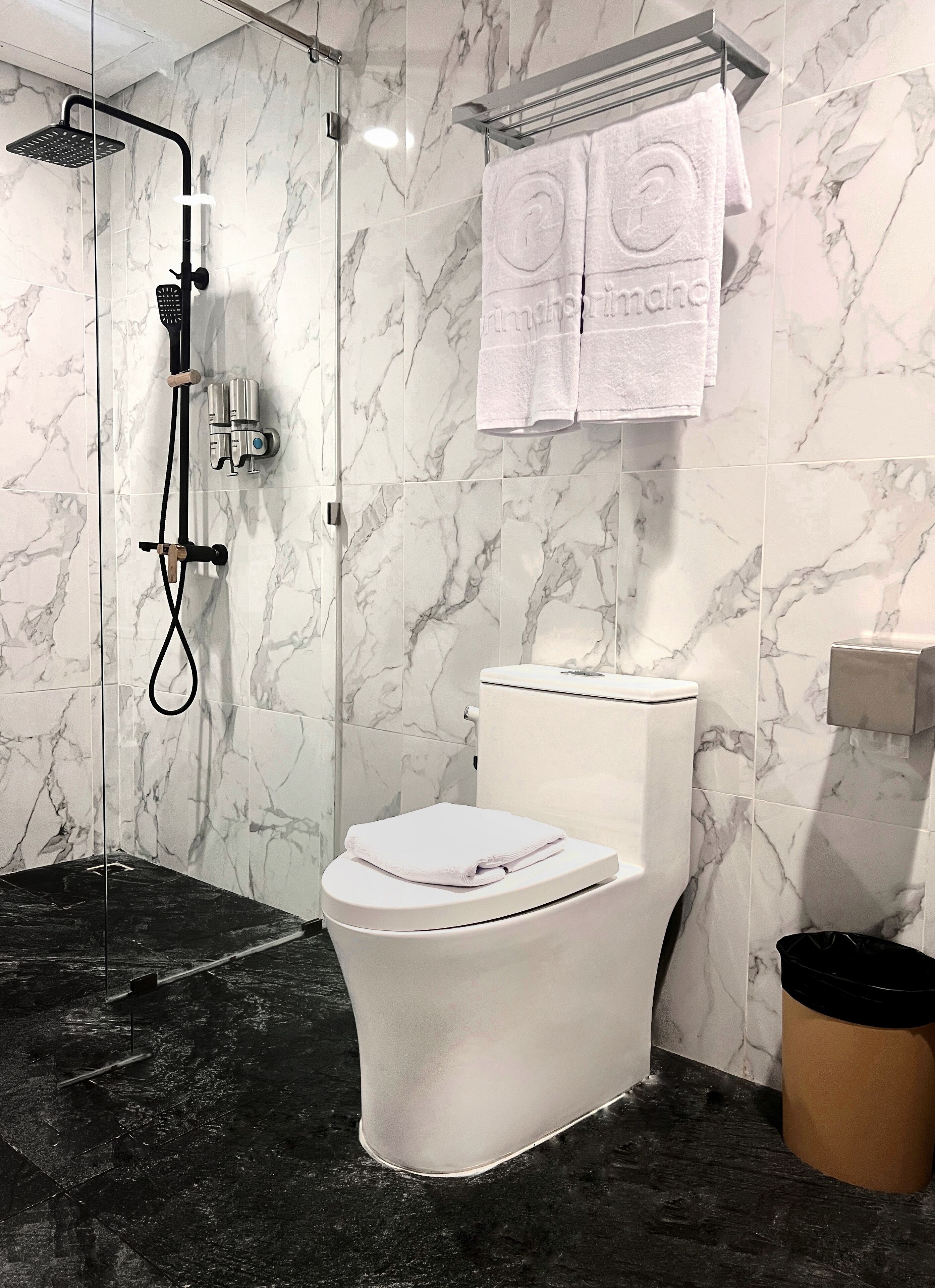 A bathroom with a white toilet, a glass-enclosed shower, and marble walls.