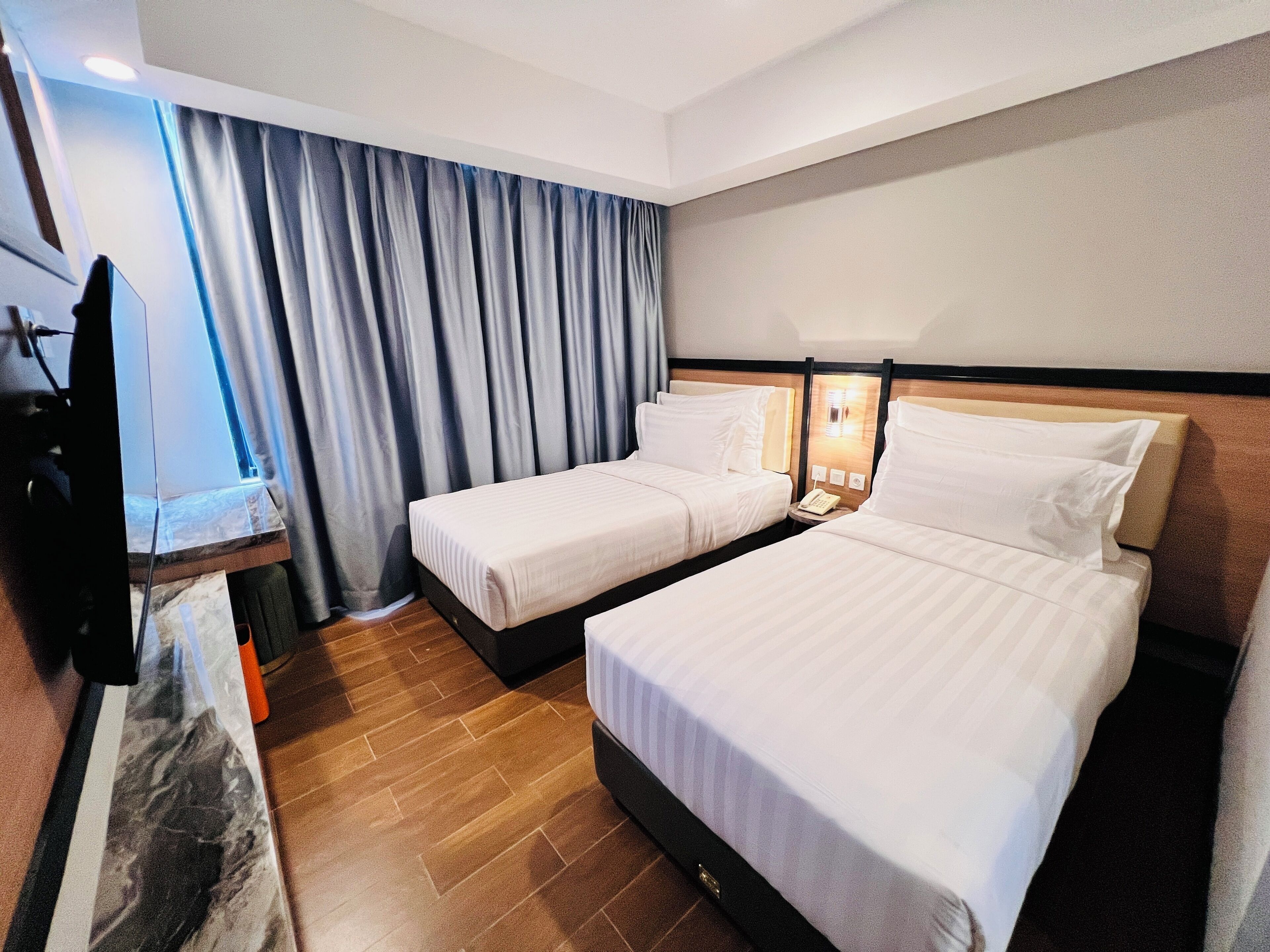 A hotel room with two beds, a desk with a chair, a TV, and a window with curtains.