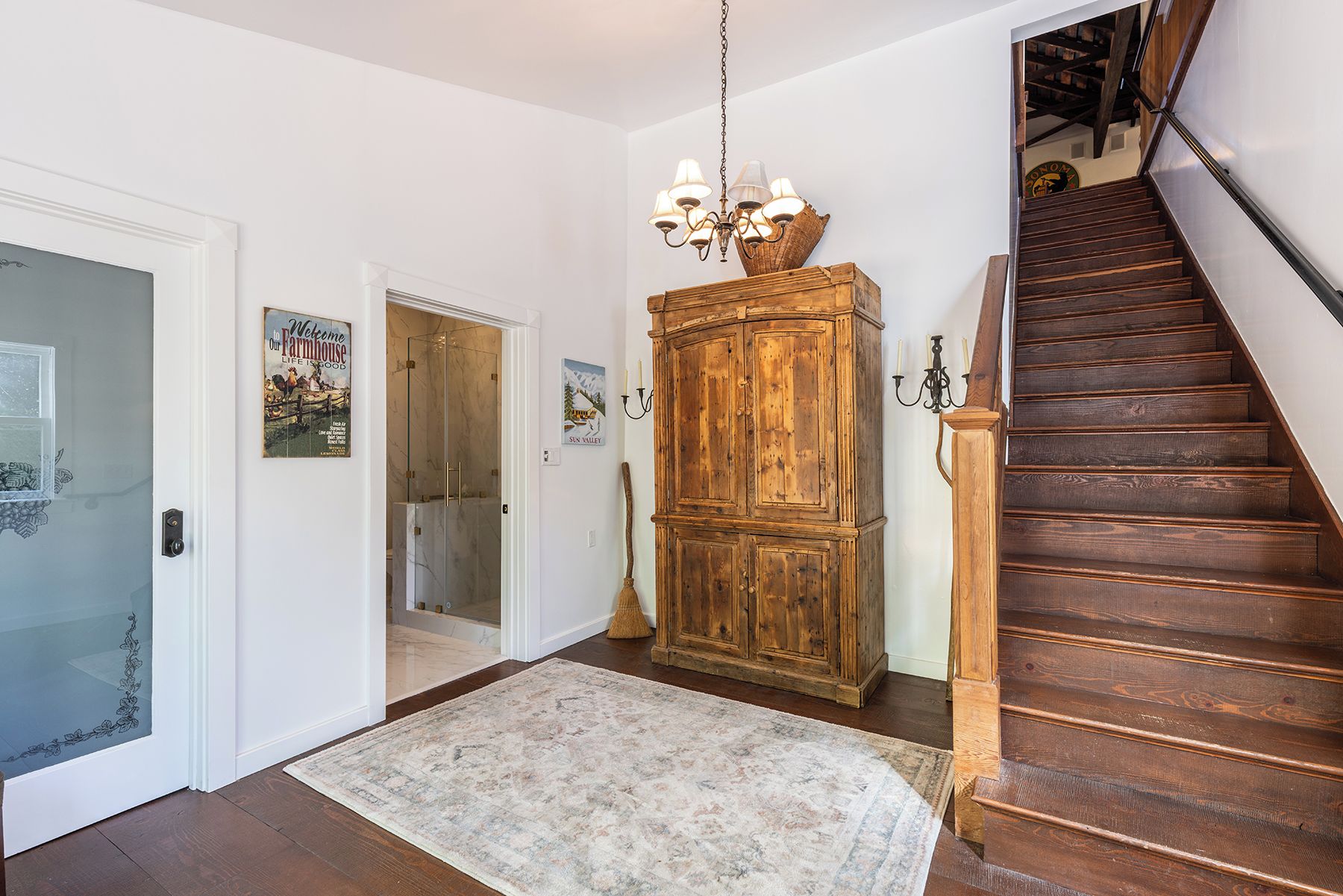 A hallway with a wooden staircase, a chandelier, a cabinet, and a rug.
