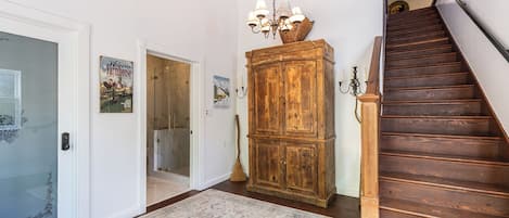 A hallway with a wooden staircase, a chandelier, a cabinet, and a rug.