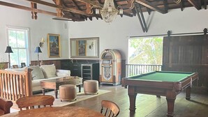 Une pièce spacieuse comprenant une table à manger en bois, des chaises, un billard et un coin salon confortable avec un canapé et des poufs.