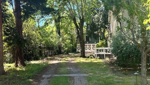 Un chemin pavé serpente à travers un jardin luxuriant, bordé d’arbres, avec un bâtiment visible au loin.