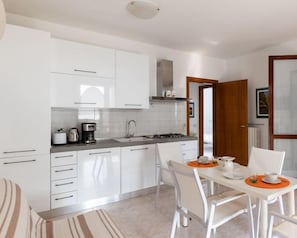 A modern kitchen with white cabinets, a dining table with chairs, and a coffee maker. - [5 Min from Lake Garda] with Free Swimming Pool (Padenghe Sul Garda)