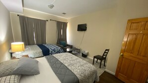 A hotel room with two beds, a desk, a chair, a TV, and a wooden door. - Cjay Homes (Jersey City)