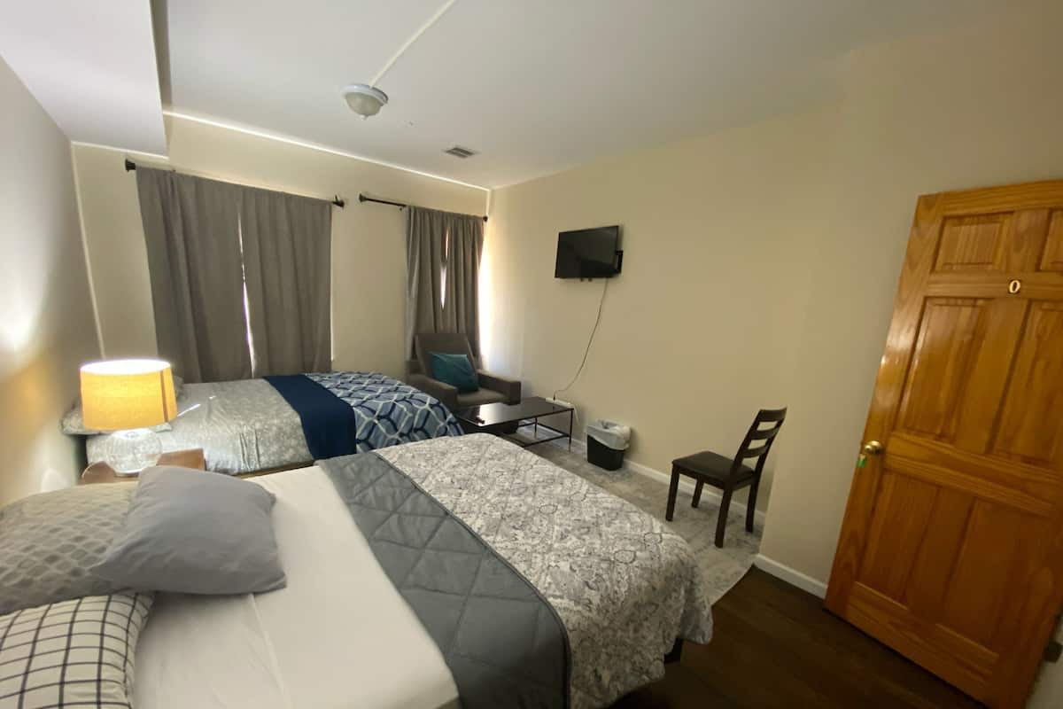 A hotel room with two beds, a desk, a chair, a TV, and a wooden door.