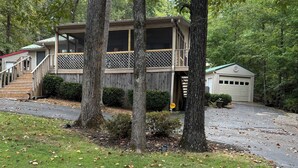 Une cabane dotée d’une terrasse, entourée d’arbres et comprenant un garage.