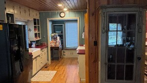 Une cuisine avec un plancher en bois, un réfrigérateur, des placards et une porte avec une fenêtre.
