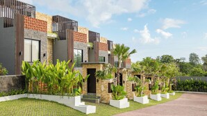 A modern residential building with a stone facade, large windows, and a well-maintained garden with various plants and a paved driveway. - Tropical Villa 8A - 8 Min Melasti Beach (Ungasan)