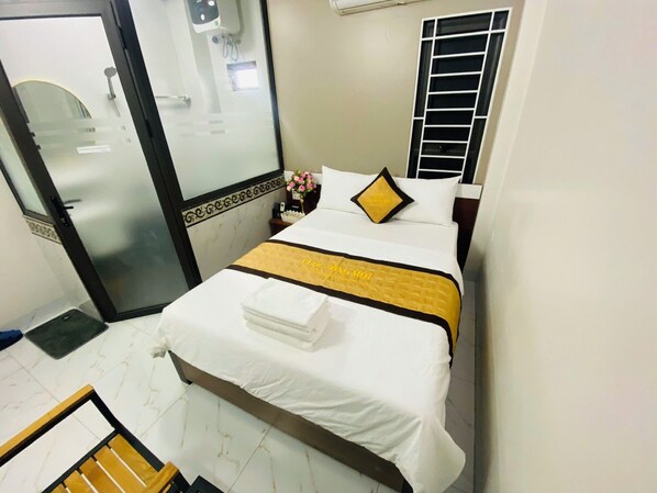 Una habitación de hotel con cama, mesita de noche, espejo, ventana con persianas y puerta.