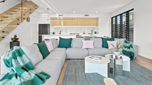 A modern living room with a grey sectional sofa, a coffee table, and a staircase with glass railings. - Salt Life Byron. Wifi, Parking & Pool in Paradise (Byron Bay)