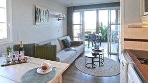 Una sala de estar moderna con un sofá, una mesa de comedor con un tapete, una zona de cocina y un balcón con mobiliario exterior.